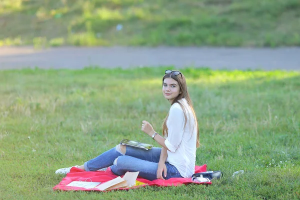 Giovane ragazza seduta sull'erba nel parco e lavora in un computer portatile e mangiare fast food — Foto Stock