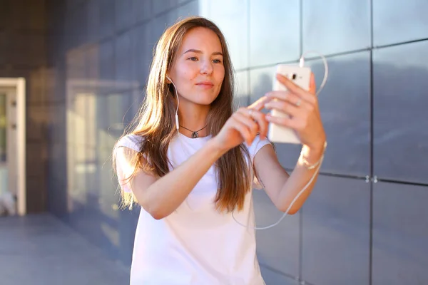 Hermosa chica joven estudiante sosteniendo el teléfono, sonriendo y c — Foto de Stock