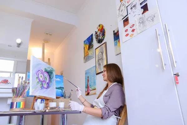 Chica se sienta en el taburete en el caballete y escribir pintura, utiliza el pincel para — Foto de Stock