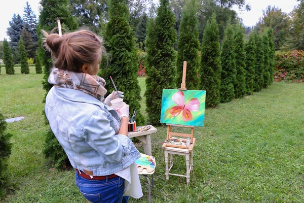 Woman artist stands with brush in hand near easel, looking and f — Stock Photo, Image