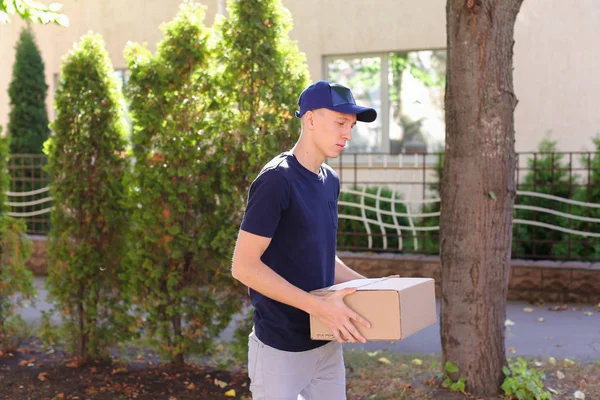 Joven mensajero llevando la orden en las manos, sonriendo a la cámara y — Foto de Stock