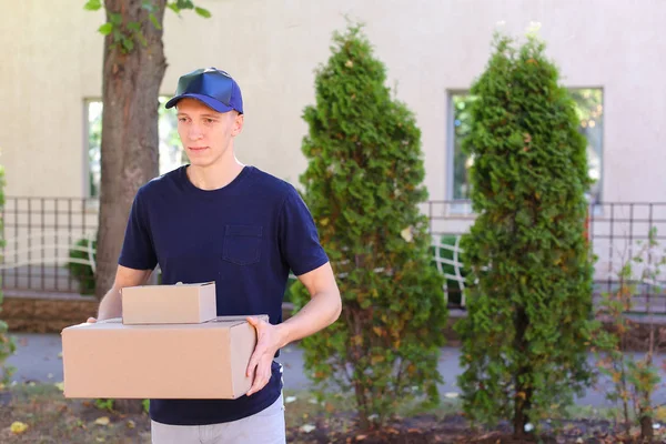 Joven mensajero llevando la orden en las manos, sonriendo a la cámara y — Foto de Stock