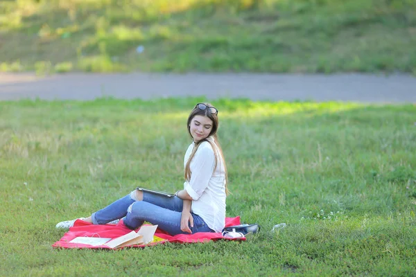 Молодая девушка сидит на траве в парке и работает за ноутбуком и ест фаст-фуд — стоковое фото