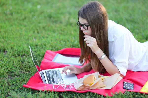 Jovem sobre a natureza de comer fast food e trabalhar em um laptop — Fotografia de Stock