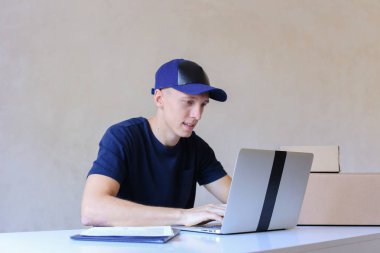 Postane bilgisayarda yazarak masada oturan kurye.