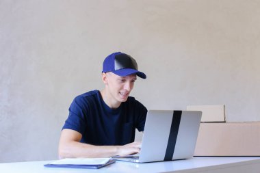 Postane bilgisayarda yazarak masada oturan kurye.