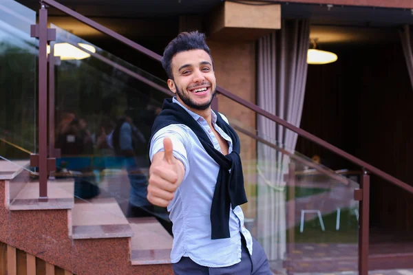 Wesoły, młody człowiek wygląda muzułmański, uśmiechając się i pokazuje gest ręki — Zdjęcie stockowe