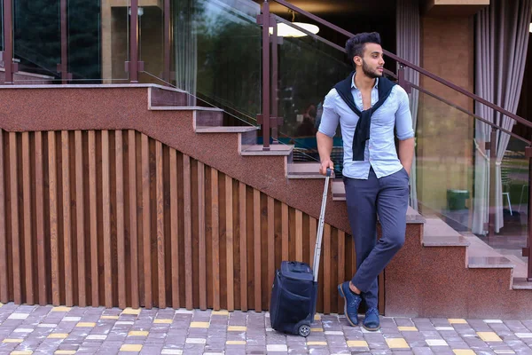 Attractive young Arabic man standing with suitcase in hand and p — Stock Photo, Image