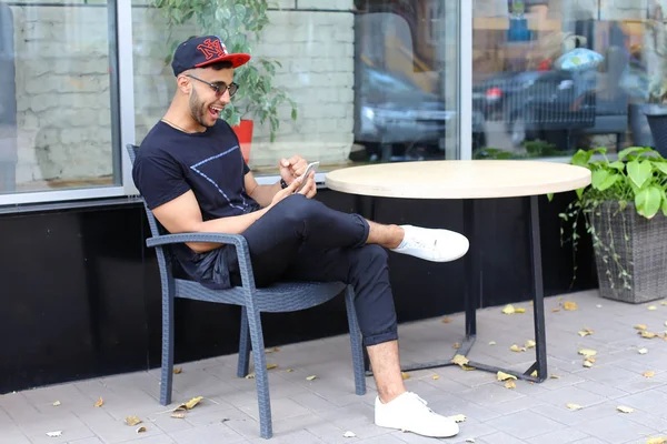 Un joven arabio guapo usa el teléfono, se sienta a charlar, se ríe — Foto de Stock