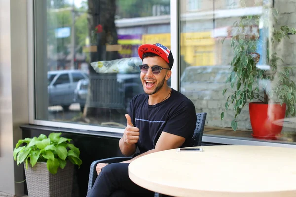 Lindo sonriente joven árabe sostiene el pulgar hacia arriba y sentado en la silla cerca — Foto de Stock