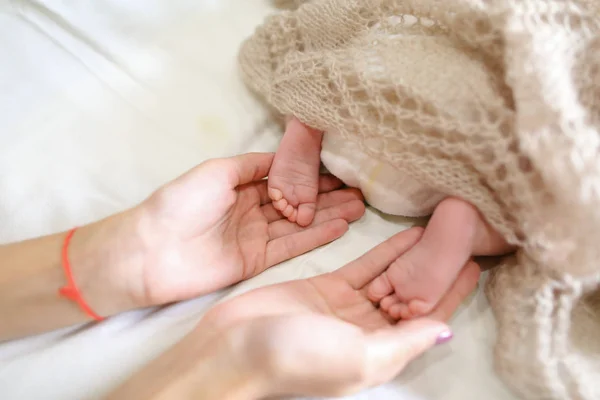 Mütter halten in den Händen winzige Füße des neugeborenen Babys, bedeckte Strickwaren — Stockfoto
