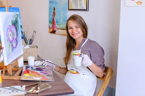 Nettes Mädchen Künstler hält Pinsel in der Hand und zeichnet, trinkt aus Becher, — Stockfoto