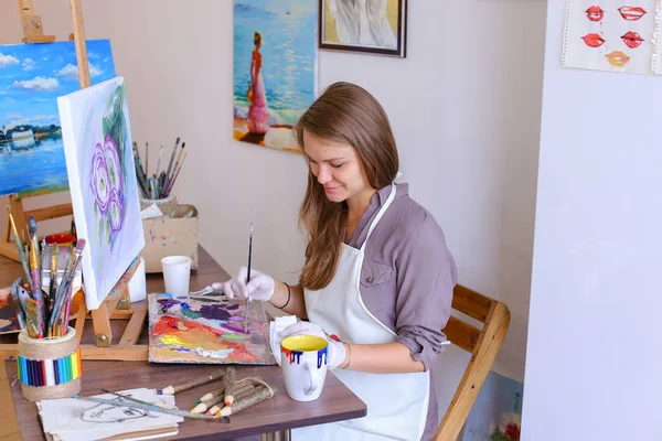 Dívka sedí na stoličce na stojan a psaní malba, používá štětec — Stock fotografie