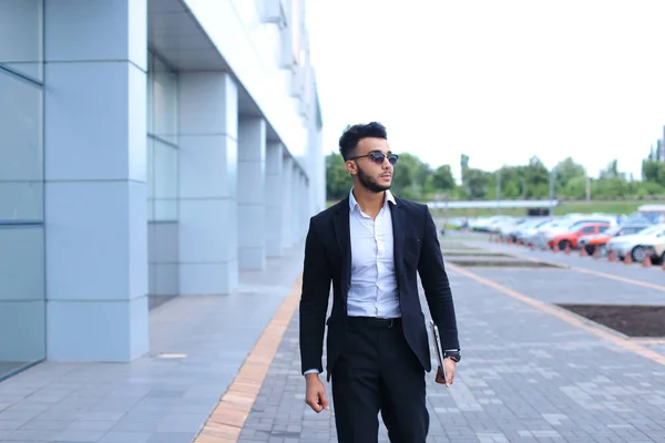 Арабский парень в бизнес-центре стоит улыбаясь ходьба медленно — стоковое фото