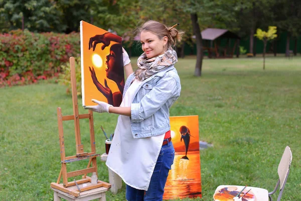 Γυναίκα καλλιτέχνης κατέχει ζωγραφική και μοιάζει σε αυτό, ποζάρουν στην κάμερα μια — Φωτογραφία Αρχείου