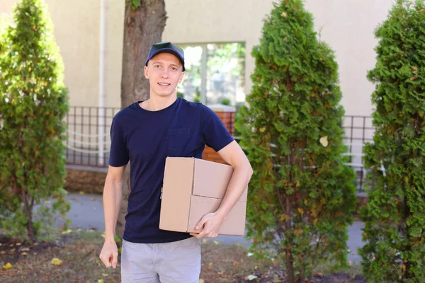 Joven mensajero llevando la orden en las manos, sonriendo a la cámara y — Foto de Stock