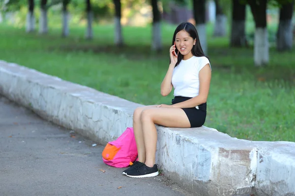 年轻的女孩坐在和谈在公园里电话 — 图库照片