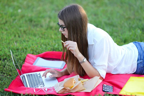 Jeune fille sur la nature de manger de la restauration rapide et de travailler à un ordinateur portable — Photo