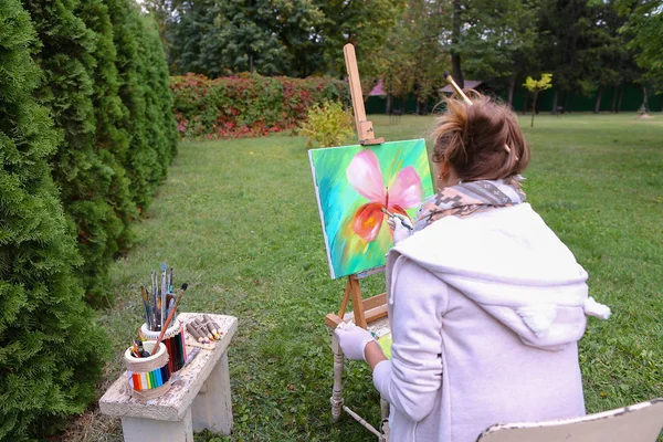 Professional artist woman writes picture sitting at easel with b