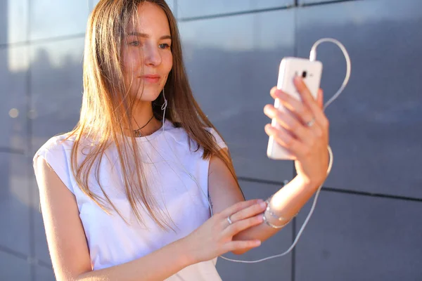 Hermosa chica joven estudiante sosteniendo el teléfono, sonriendo y c — Foto de Stock