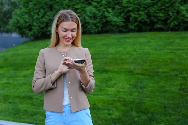 Hermosa mujer mirando la pantalla del teléfono inteligente y sonríe, se para — Foto de Stock