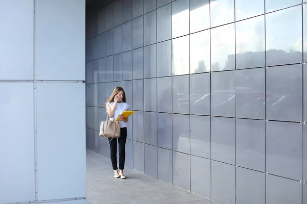 Σοβαρή επιχειρηματική νεαρή γυναίκα περπατά και να μιλά στο τηλέφωνο, κατέχει και — Φωτογραφία Αρχείου