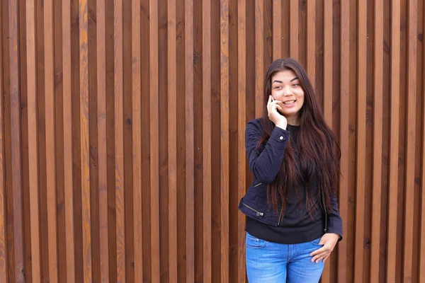 Beautiful dark-haired woman holds in hand phone and talking, smi — Stock Photo, Image