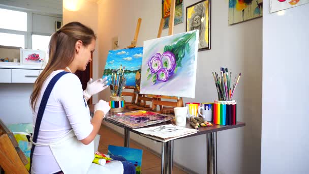 Artista menina coloca em luvas e preparar pintura para uso em estúdio de arte com paredes brancas em que pendurar Pictures . — Vídeo de Stock