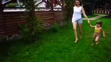 Genç anne ve bebek kız çimenlerin üzerinde koşturup ve açık havada gündüz üsteki dinlenmek için elele eğleniyor.