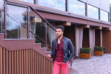 Çekici genç Arap adam etrafına bakıyor ve elini kolunu sallaya dönüyor, gülümser bir