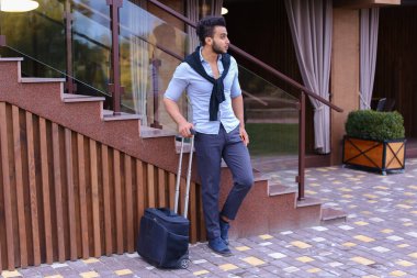 Çekici genç Arap adam elinde bavulla ayakta ve p