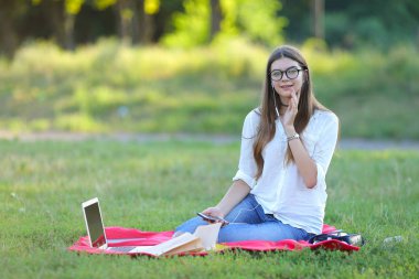 gülümseyen ve onun laptop müzik çalışma parkta oturan genç kız