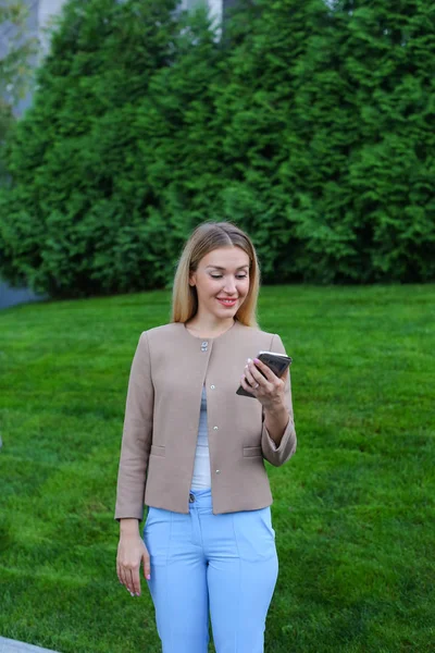 Hermosa mujer mirando la pantalla del teléfono inteligente y sonríe, se para — Foto de Stock