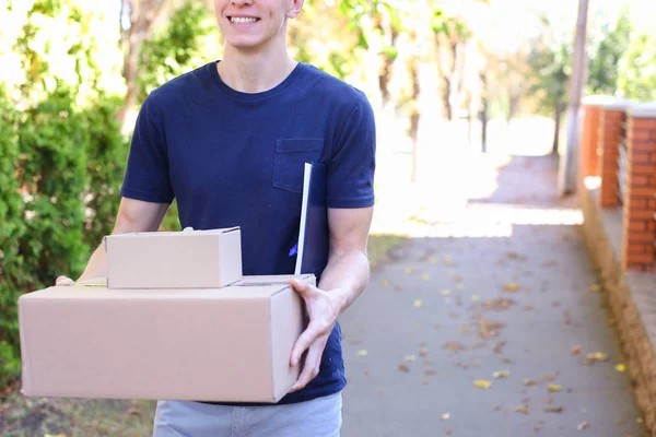 Cartero llevando un paquete en las manos sonriendo a la cámara en segundo plano — Foto de Stock