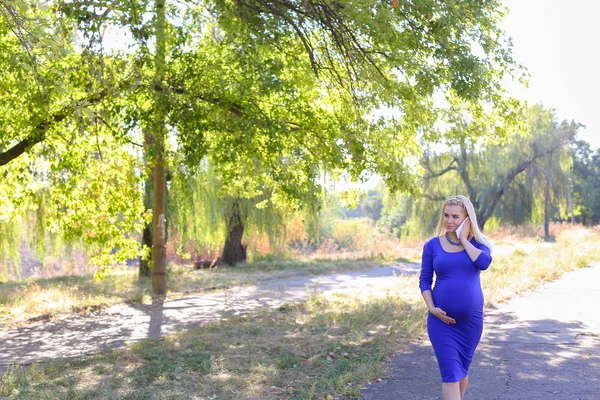 Elegante schwangere Frau geht und redet über Gadget auf der Straße entlang — Stockfoto