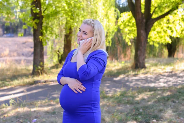 Mujer embarazada elegante va y hablando en Gadget en el camino a lo largo de — Foto de Stock