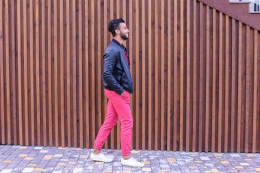 Çekici genç Arap adam etrafına bakıyor ve elini kolunu sallaya dönüyor, gülümser bir