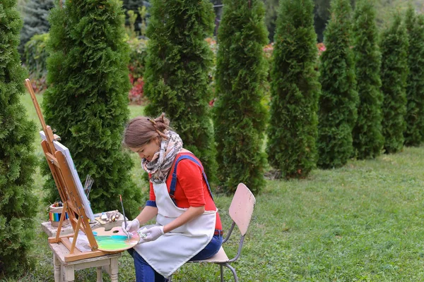 Dívka umělec maluje obraz a sedí na židli u stojanu stranách t — Stock fotografie