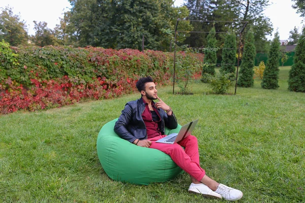 Schöner arabischer junger Geschäftsmann sitzt mit Laptop im Stuhl, schaut — Stockfoto