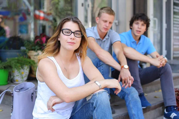 Young three friends sitting floor in the street, talking, using — Stock Photo, Image