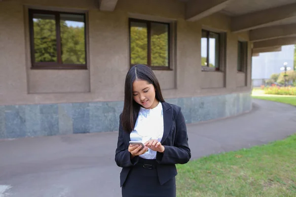 Krásná mladá Asijská studentka drží telefon, usmíval se a — Stock fotografie