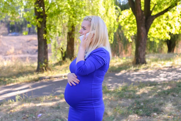 Tyylikäs raskaana oleva nainen menee ja puhuu Gadget tiellä pitkin — kuvapankkivalokuva