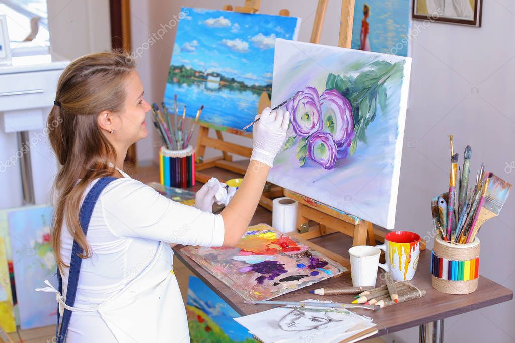 Girl artist sits with back to camera and draws oil picture with