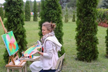 Kız sanatçı boya resim ve t kenarlarında şövale sandalyeye oturur