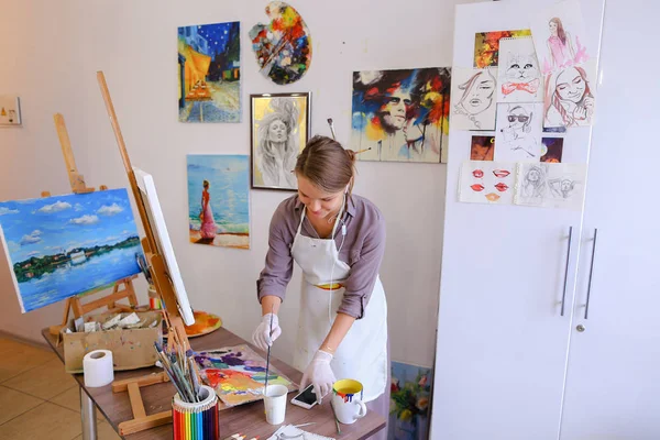 Beautiful young painter paints picture uses brushes and oil, and