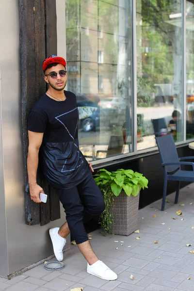 Handsome young man arab stands near wall smiles, rejoices and ho