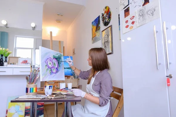 Girl Sits on Stool at Easel And Writing Painting, Uses Brush to