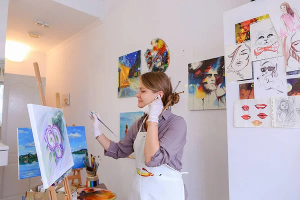 Beautiful young painter paints picture uses brushes and oil, and