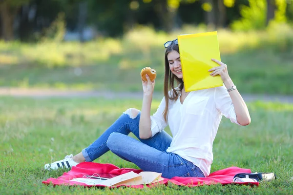 young girl sitting on the grass in the park and works at a laptop and eating fast food