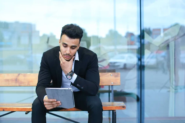 Man in suit arabic puts on sunglasses with tablet near business